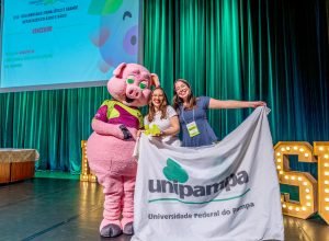 Pamela e Beatriz com o prêmio, ao lado do mascote do Intercom Sul 2026, Rabicó. Foto: Intercom